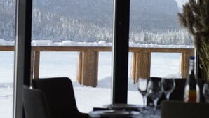 A dining area with a view of a snowy landscape through large windows. - Le Grand R (Saint Donat)