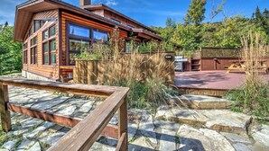 A log cabin with a stone patio, a barbecue area, and a wooden deck. - Le Grand R (Saint Donat)