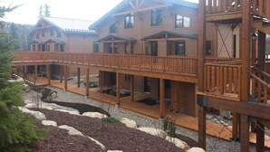 A multi-story wooden building with a covered walkway and outdoor seating areas. - Le Grand R (Saint Donat)