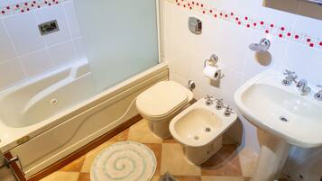 Een badkamer met een bad, toilet, bidet, wastafel en douchegordijn.