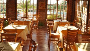 Ein Restaurant mit Backsteinwänden, Holzbalkendecken und großen Fenstern mit Blick auf einen Pool. Tische sind mit Stühlen und Tischdecken gedeckt.