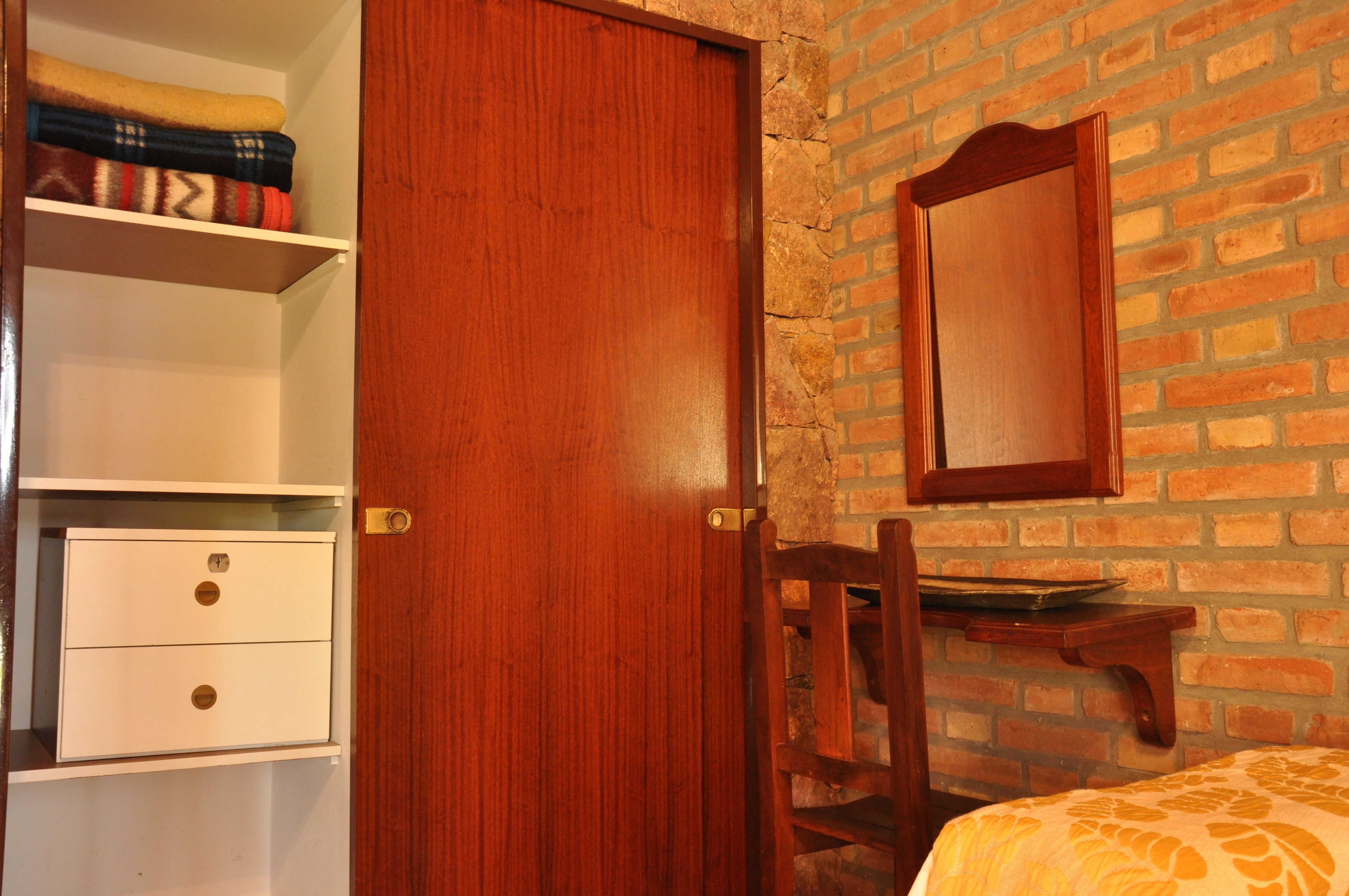 A room with a wooden door, a brick wall, a white dresser with drawers, and a mirror on the wall.