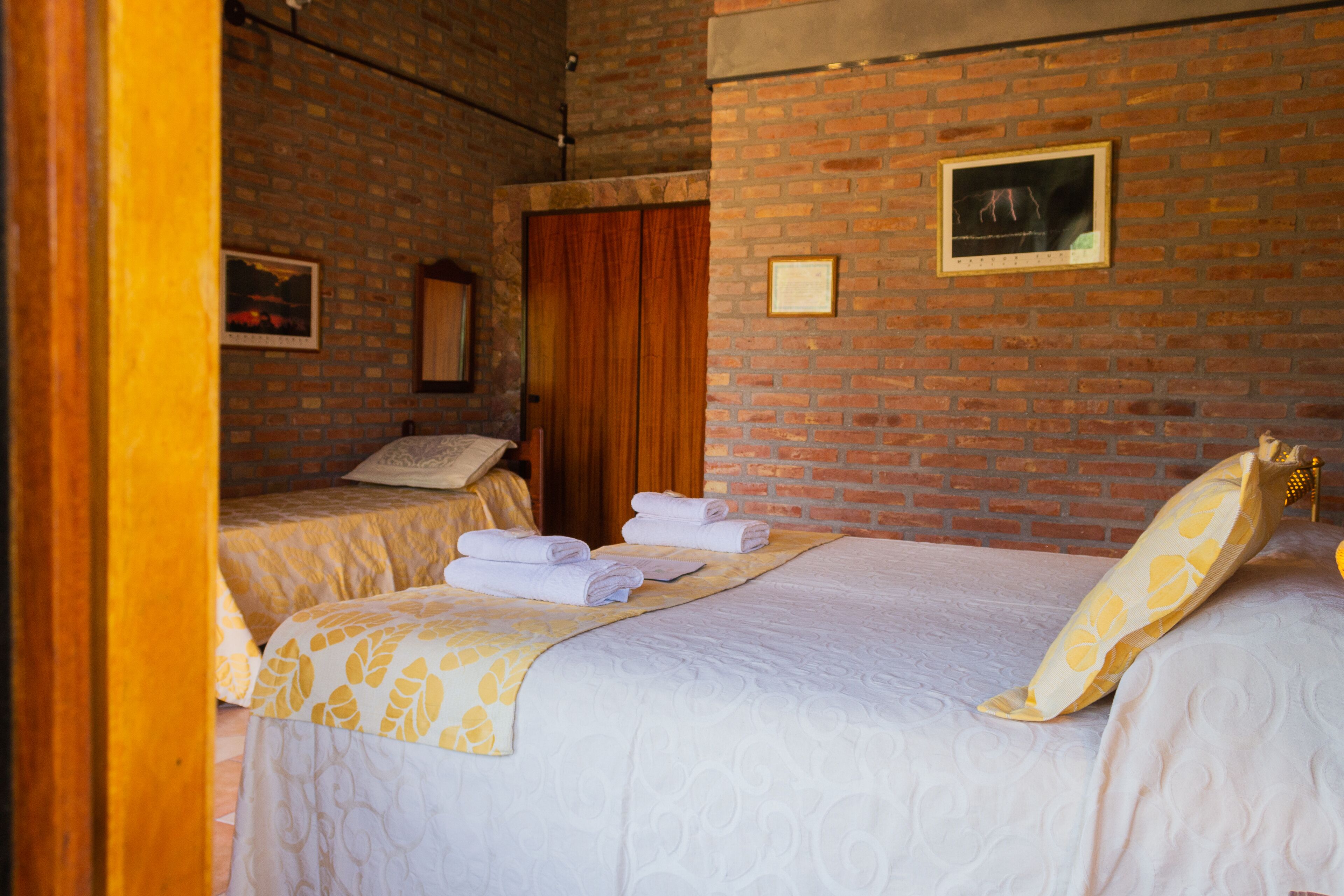 A hotel room with two beds, a brick wall, a framed picture, and a wooden door.