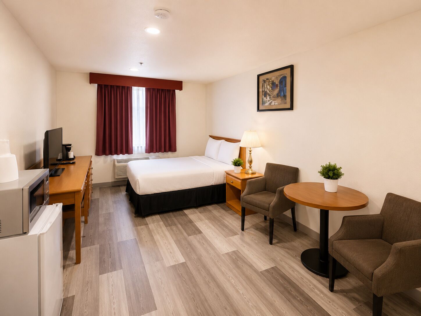 Habitación de hotel con cama, escritorio, silla, mesa y una pequeña planta en maceta.