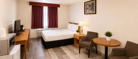 Habitación de hotel con cama, escritorio, silla, mesa y una pequeña planta en maceta.