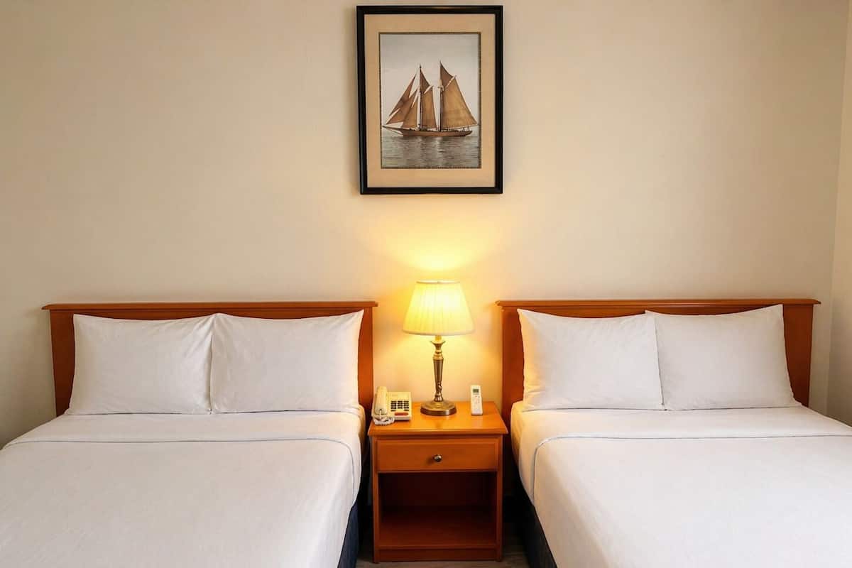 A hotel room with two beds, a nightstand with a lamp, a phone, and a framed picture on the wall.