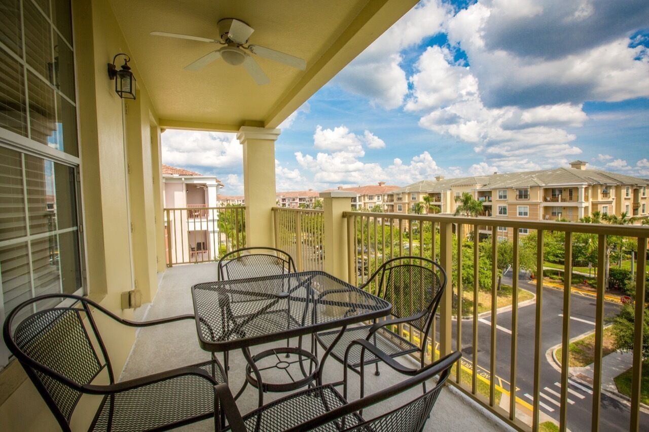 A balcony with a table and chairs, a ceiling fan, and a view of a residential area with apartment buildings.