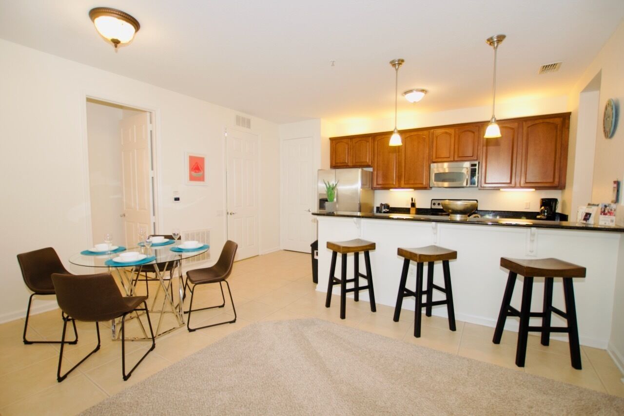 A compact kitchen with wooden cabinets, a stainless steel refrigerator, and a microwave. There is a dining area with a round table and four chairs.
