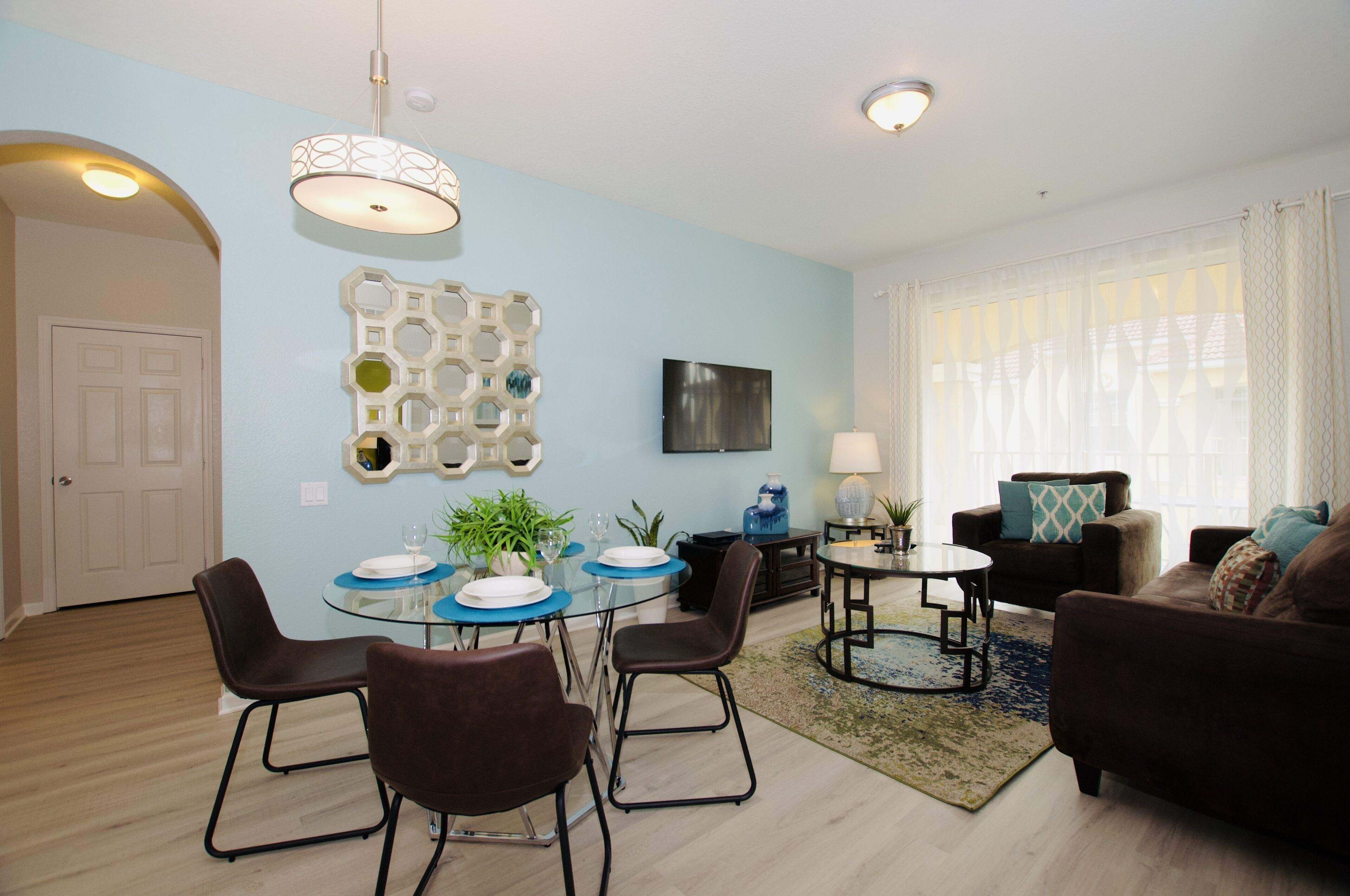 A modern living room with a dining area, featuring a round table, chairs, a sofa, and a TV.