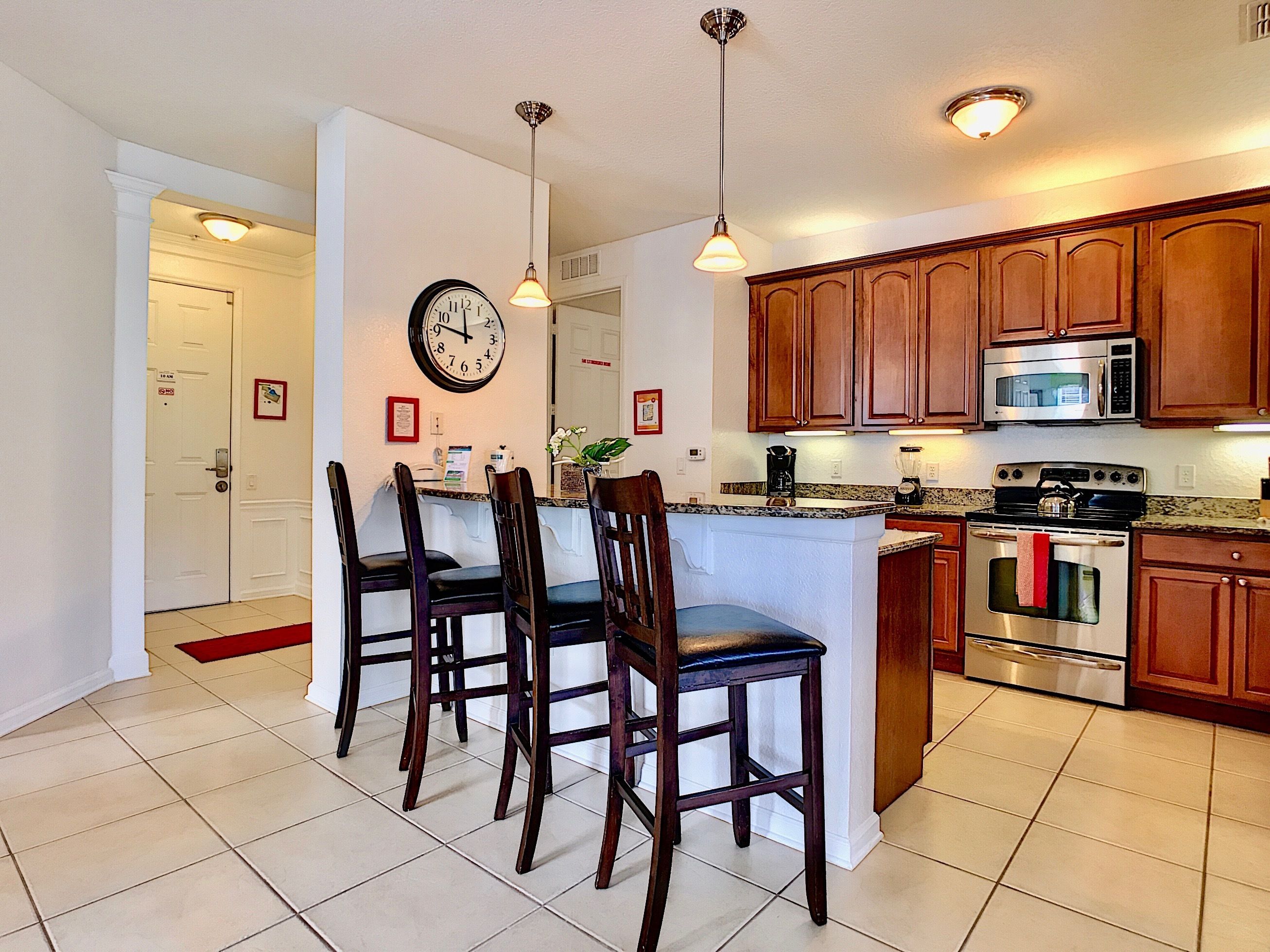 A kitchen with wooden cabinets, a stainless steel oven, and a microwave. There are three wooden chairs around a central island with a sink.