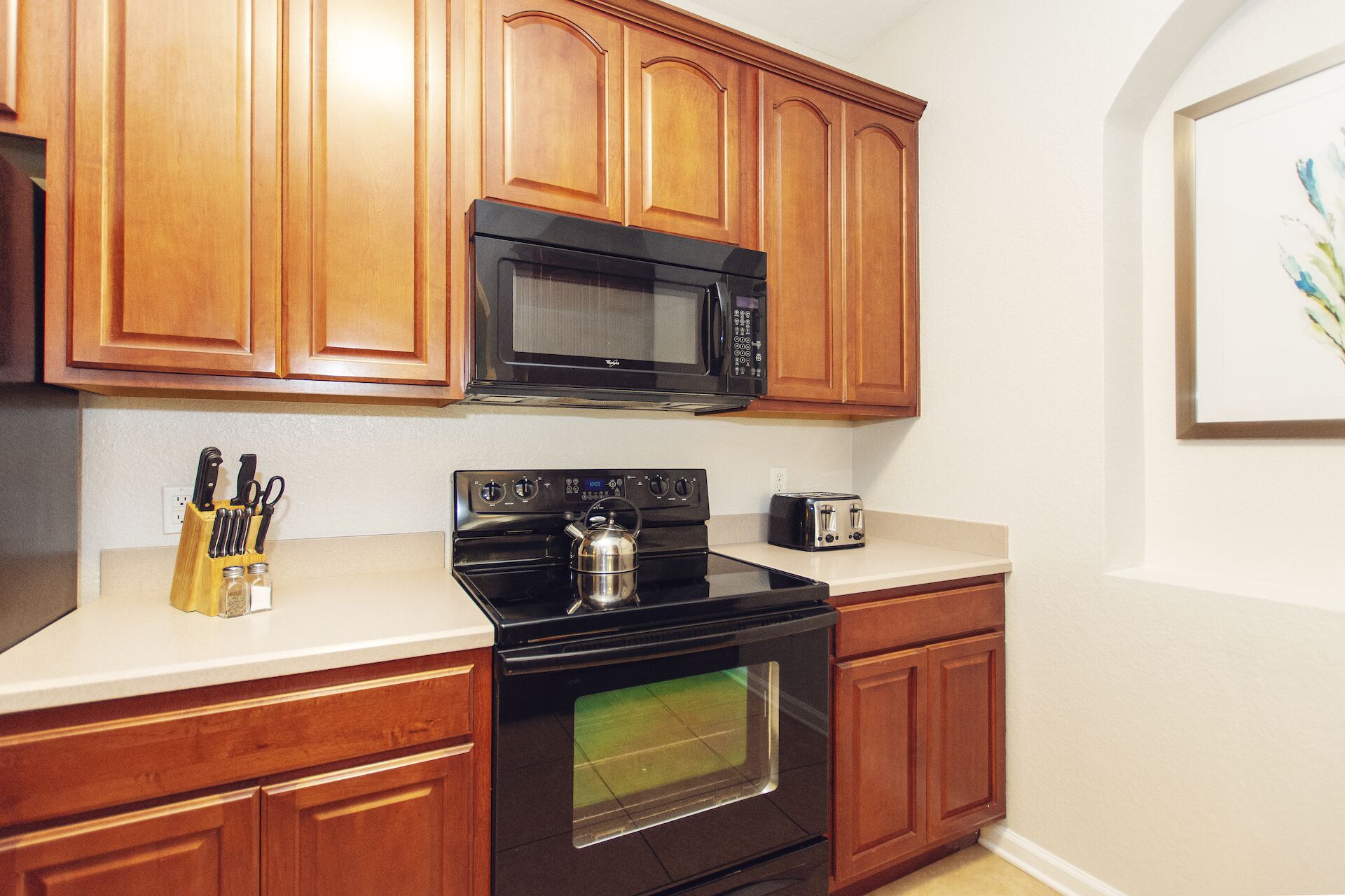 A kitchen with wooden cabinets, a black microwave, a stove, and a toaster.