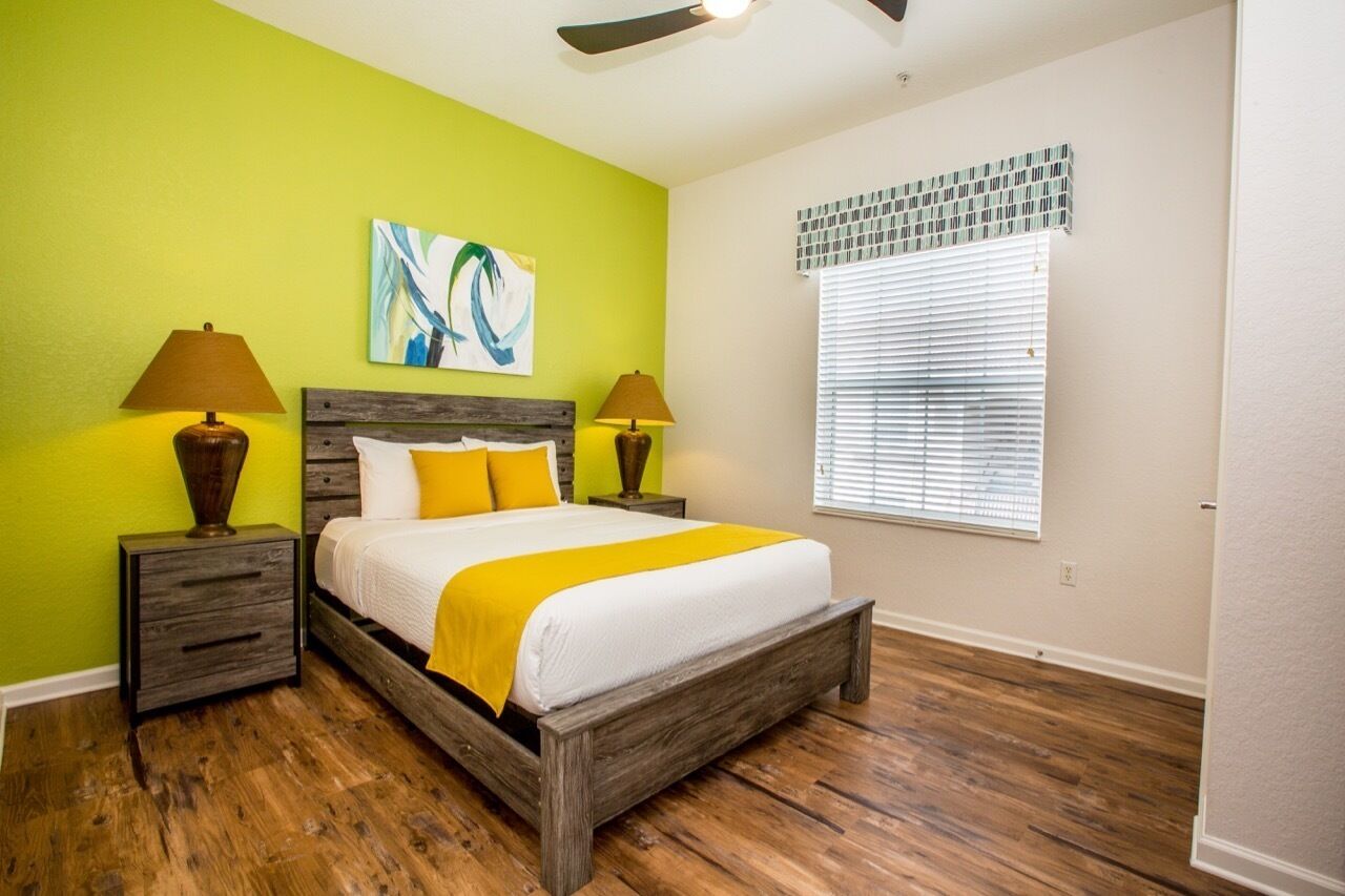 A bedroom with a wooden bed, two nightstands, a ceiling fan, a window with blinds, and a green wall.
