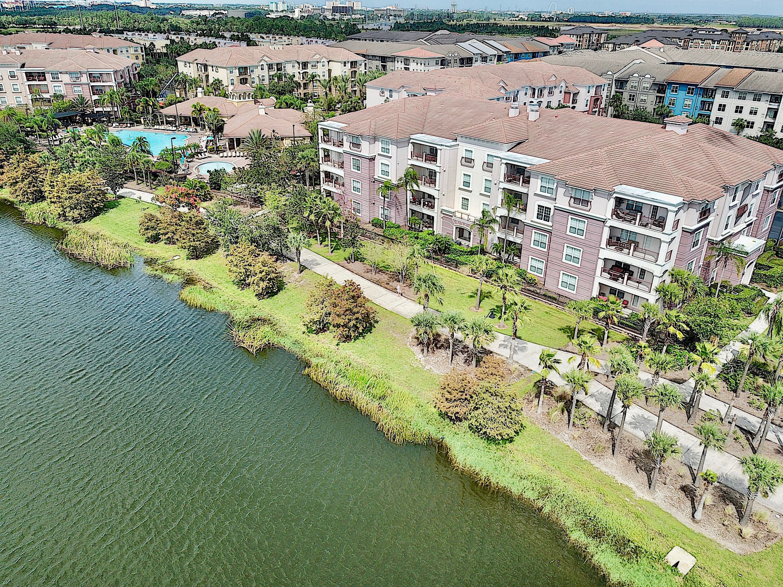 A multi-story residential building with balconies, a swimming pool, and a landscaped area with palm trees.