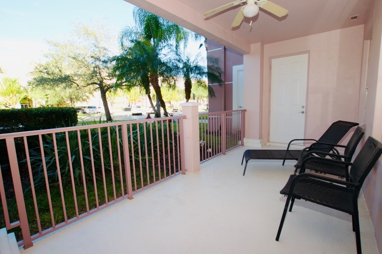 A balcony with a white ceiling fan, a door, and two black chairs.
