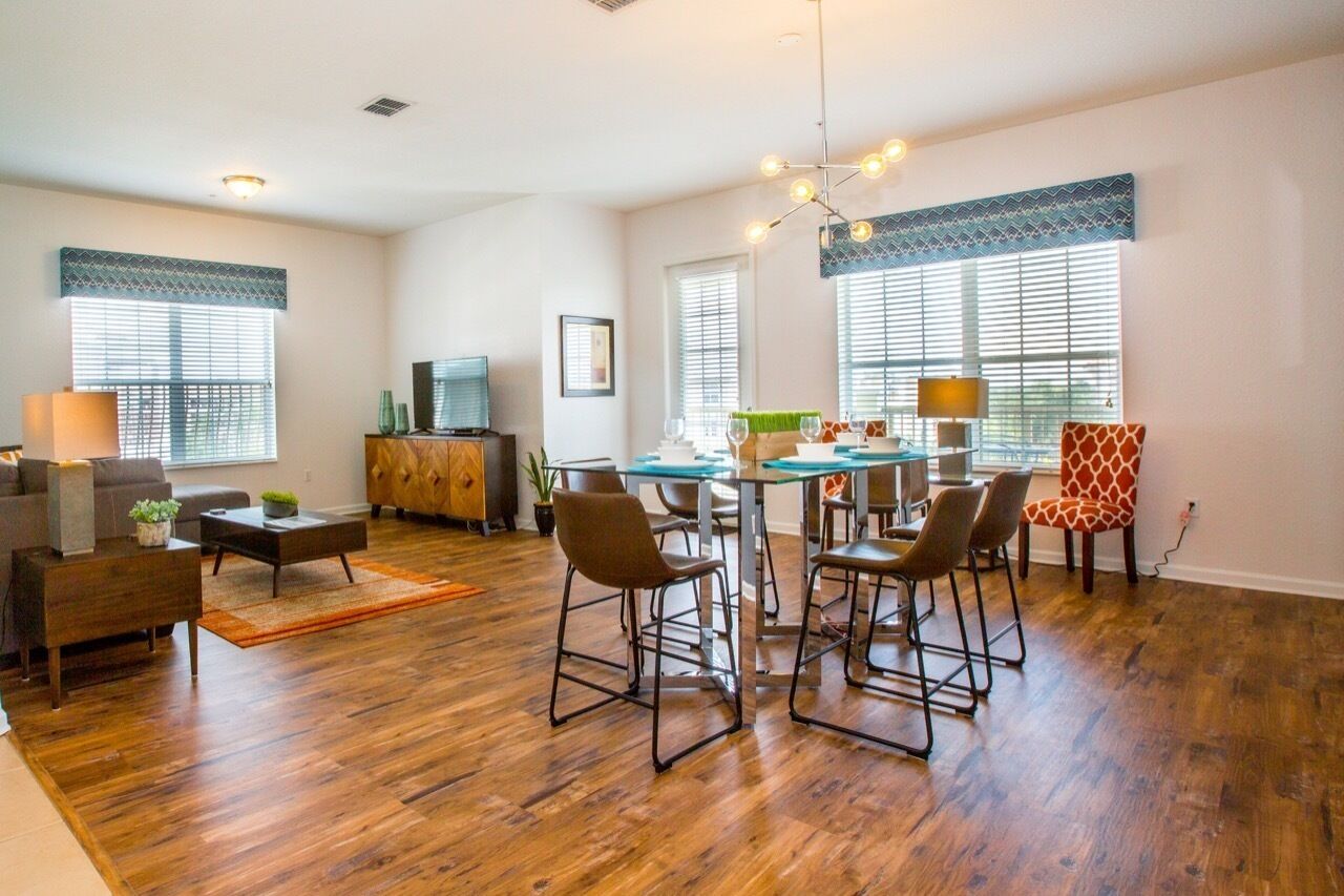 A spacious living room with a wooden floor, a sofa, a coffee table, and a TV. There is a dining area with a table and chairs.