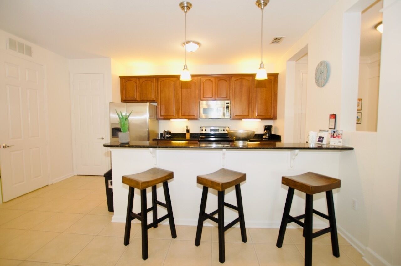 A kitchen with wooden cabinets, a stainless steel refrigerator, a microwave, and a stove. There are three wooden stools at the counter.