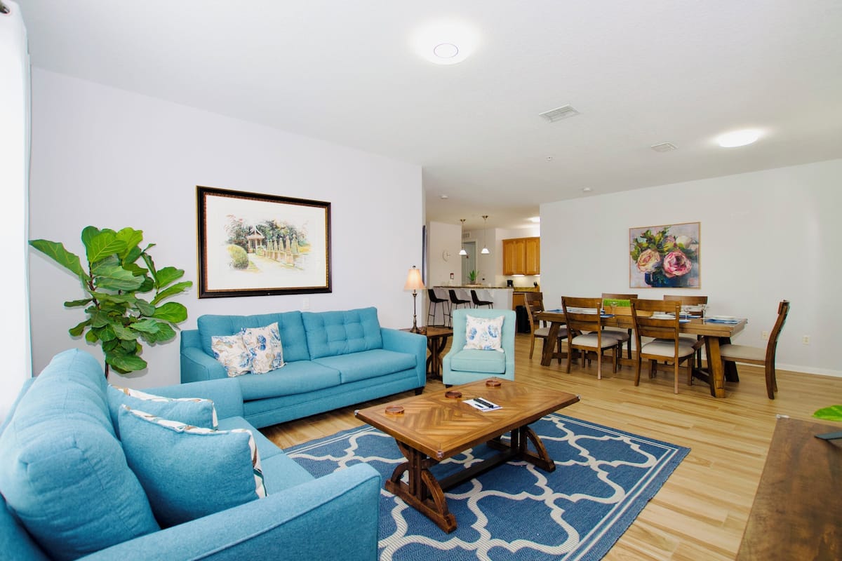 Una sala de estar con un sofá azul, una mesa de centro y una zona comedor con sillas y una mesa de madera.