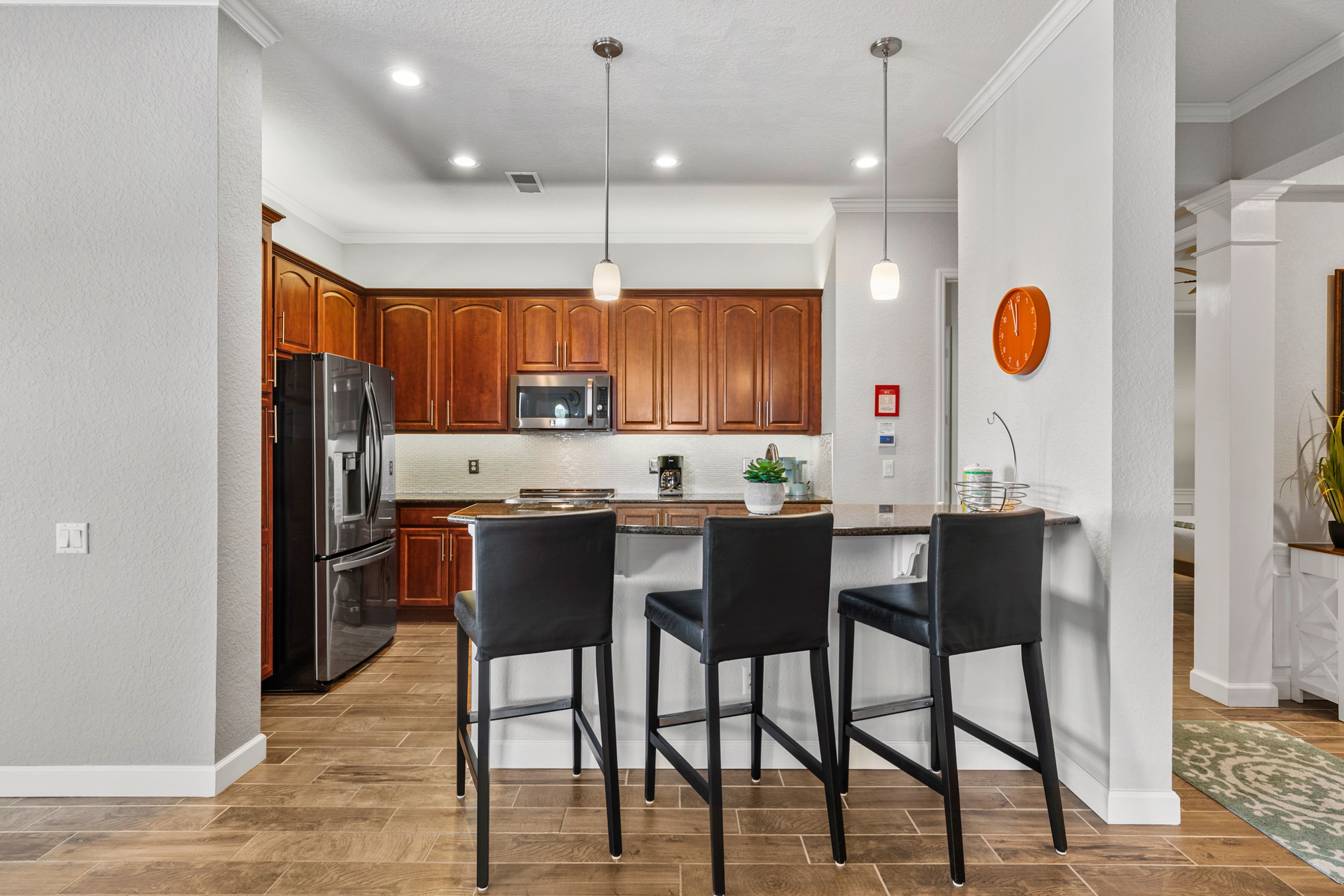 A modern kitchen with wooden cabinets, stainless steel appliances, and black bar stools.