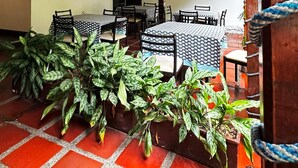 Quarto com vigas de madeira no teto, toalhas de mesa estampadas e plantas em vasos.