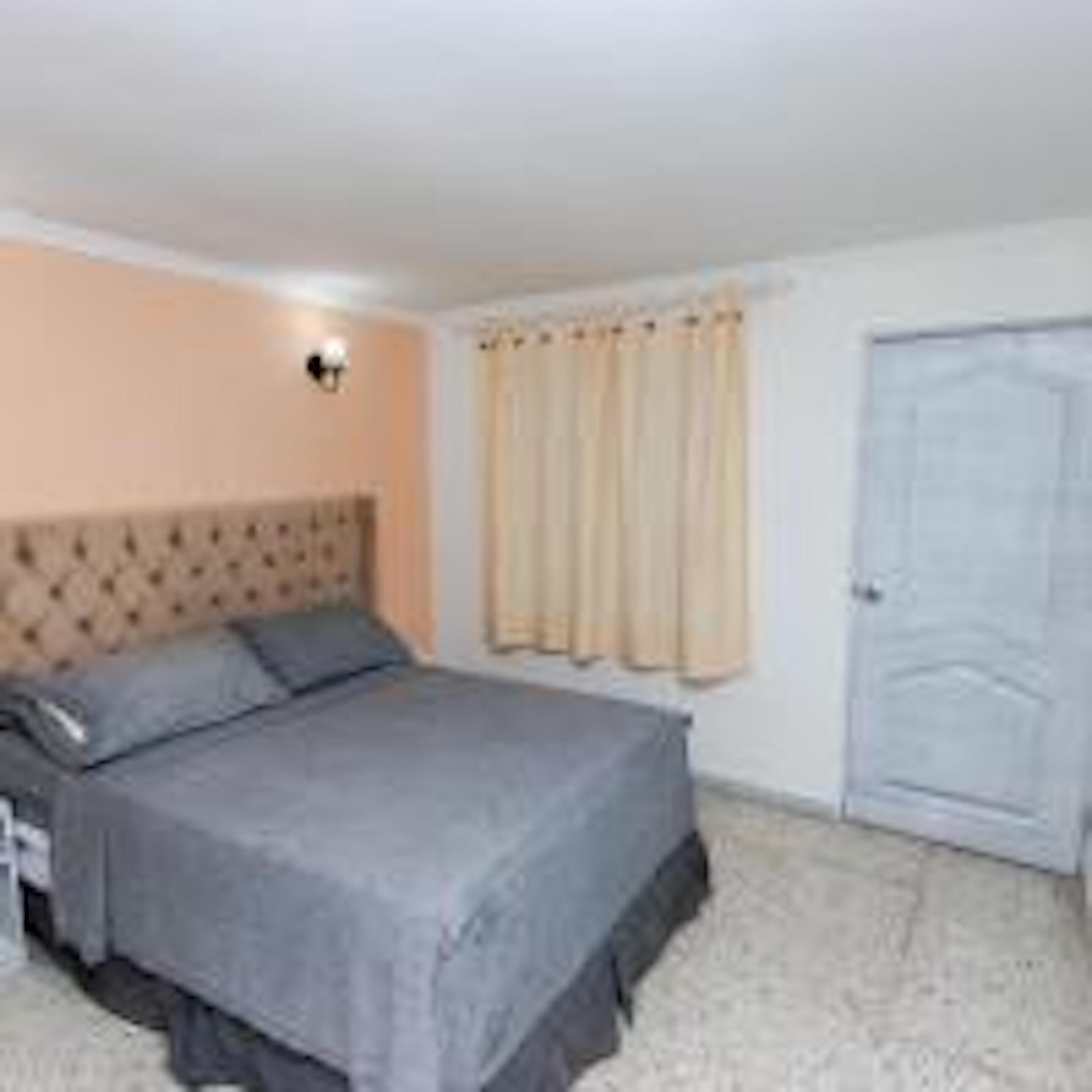 A bedroom with a bed, a nightstand, a wall-mounted lamp, and a door.