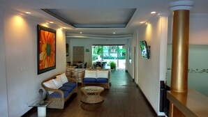 Um saguão moderno de hotel com um sofá, cadeiras, uma TV e uma janela grande.