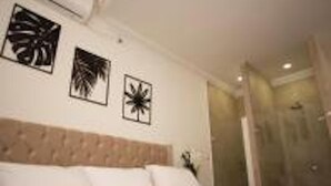 Quarto de hotel com uma cama, cabeceira e três quadros pendurados na parede.