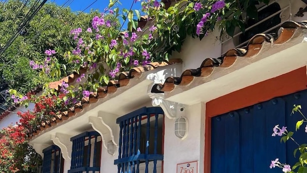 Un bâtiment avec des portes et des fenêtres bleues, une façade blanche et une enseigne sur laquelle on peut lire « Zana ».