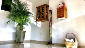 Un couloir avec une plante en pot, une armoire en bois, une grande sculpture en bois et un panier en osier.