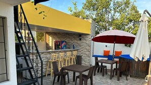Une terrasse extérieure dotée d’un bar, d’un sol en pierre et d’un escalier menant à un niveau supérieur.