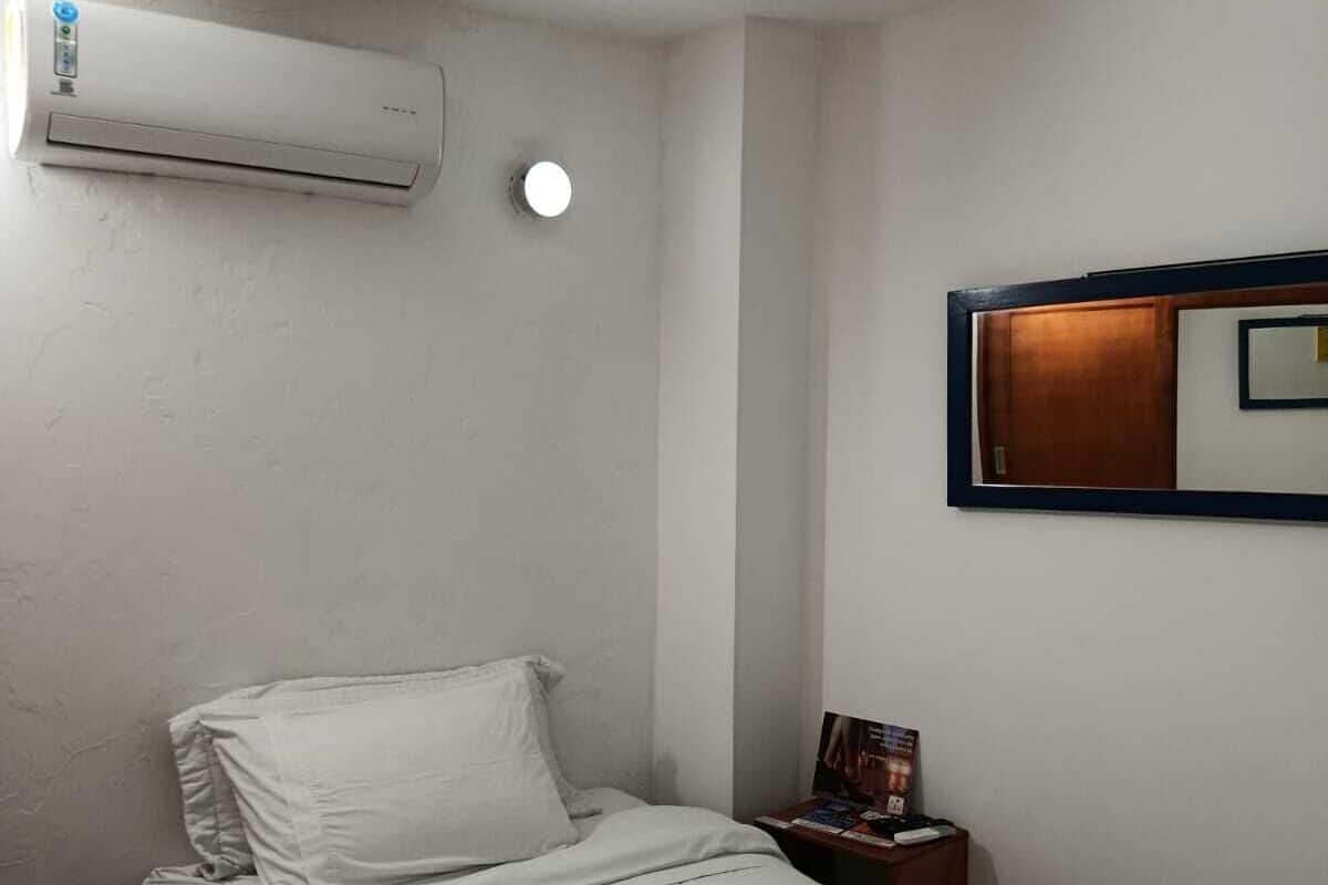 Ein Hotelzimmer mit einem Bett, einem Nachttisch, einer Klimaanlage und einem an der Wand befestigten Spiegel.