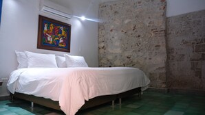 Une chambre à coucher avec un lit, du linge de lit blanc, un tableau coloré, un mur en pierre et un sol à carreaux verts.