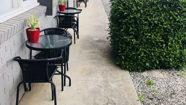 An outdoor patio with tables and chairs, potted plants, and a hedge. - Horsham Motel (Horsham)