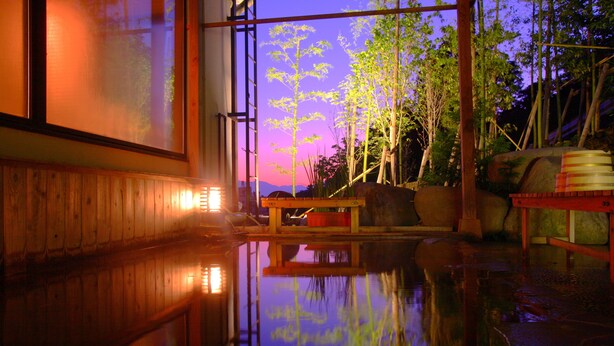 Een traditionele Japanse onsen met houten inrichting en uitzicht op bamboebomen bij zonsondergang.