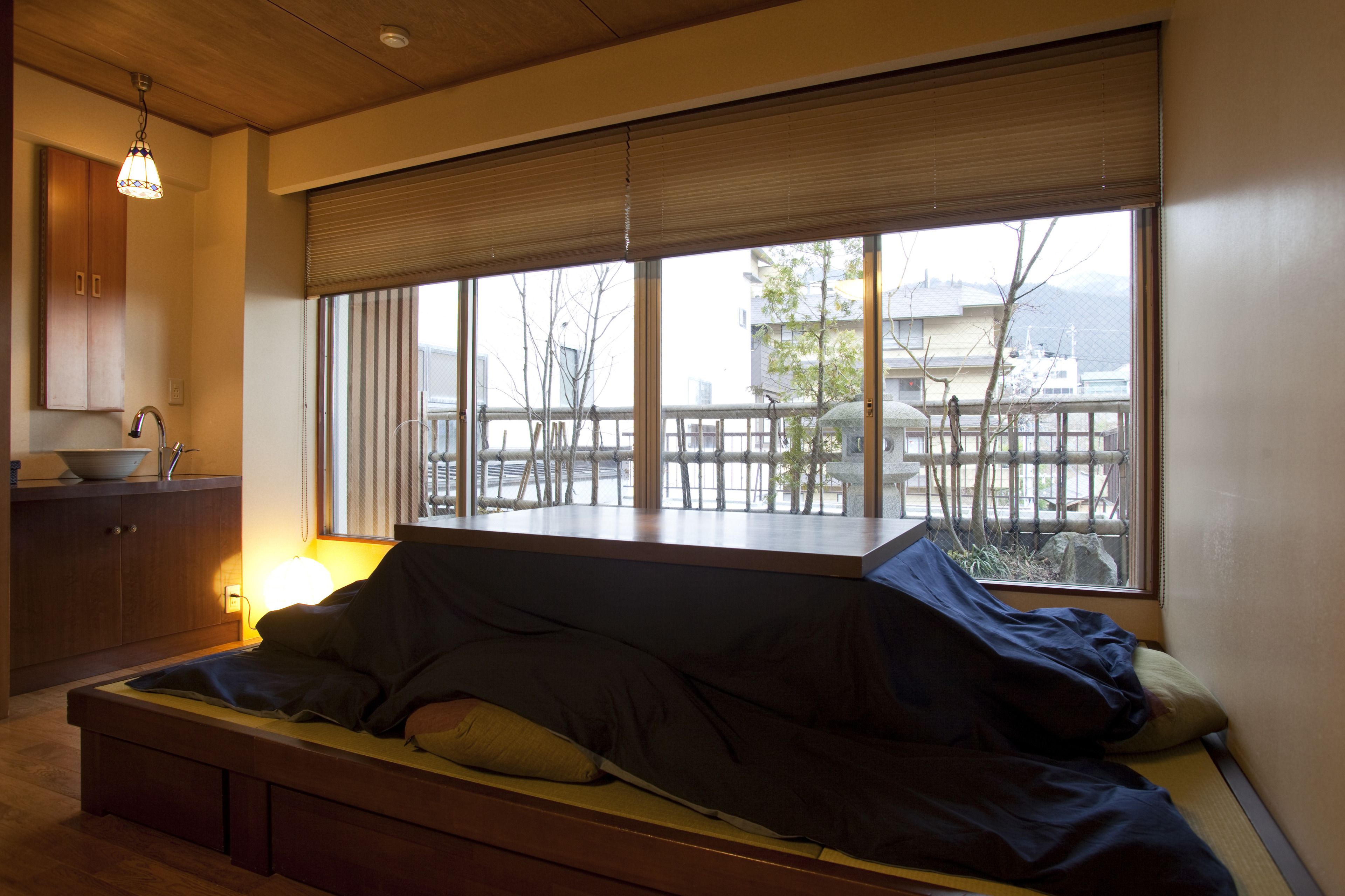 A room with a bed, a window with blinds, a wooden cabinet, and a hanging light fixture.