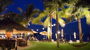 A beachside bar area with tables and chairs, palm trees, and a thatched-roof structure. - Mali Resort Pattaya Beach Koh lipe (Koh Lipe)