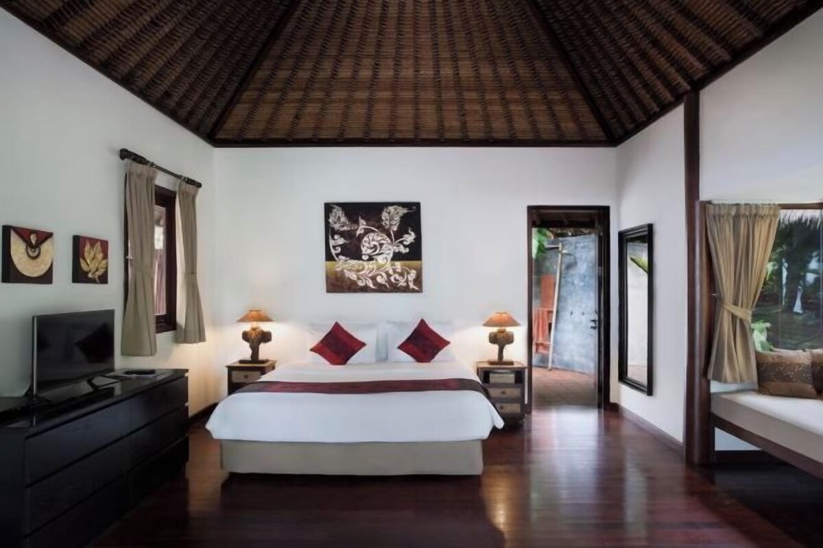 Een slaapkamer met een groot bed, bedlampjes, een televisie en kunstwerken aan de wanden.