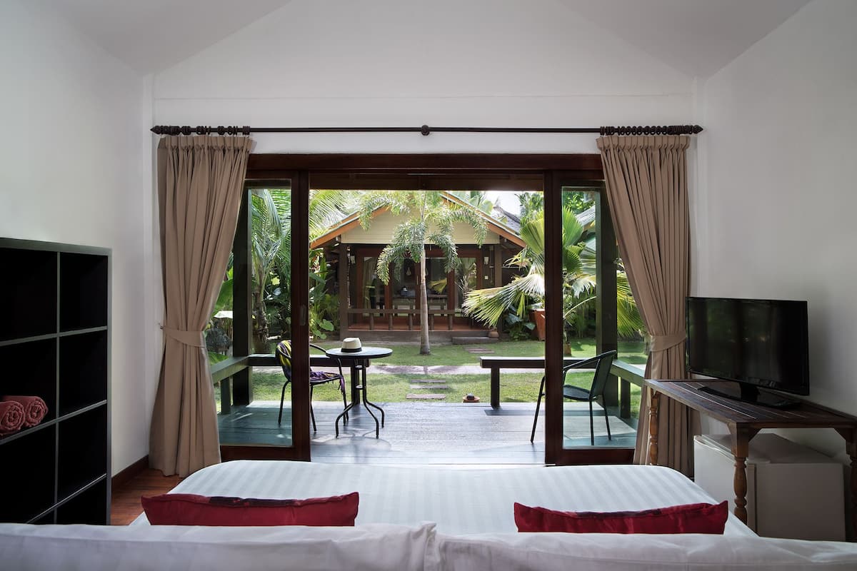 Ein Schlafzimmer mit Bett, Fernseher und Blick auf eine Terrasse mit Tisch und Stühlen.