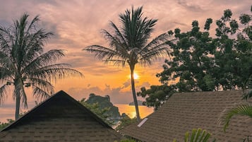 A sunset view with palm trees and traditional thatched-roof huts.