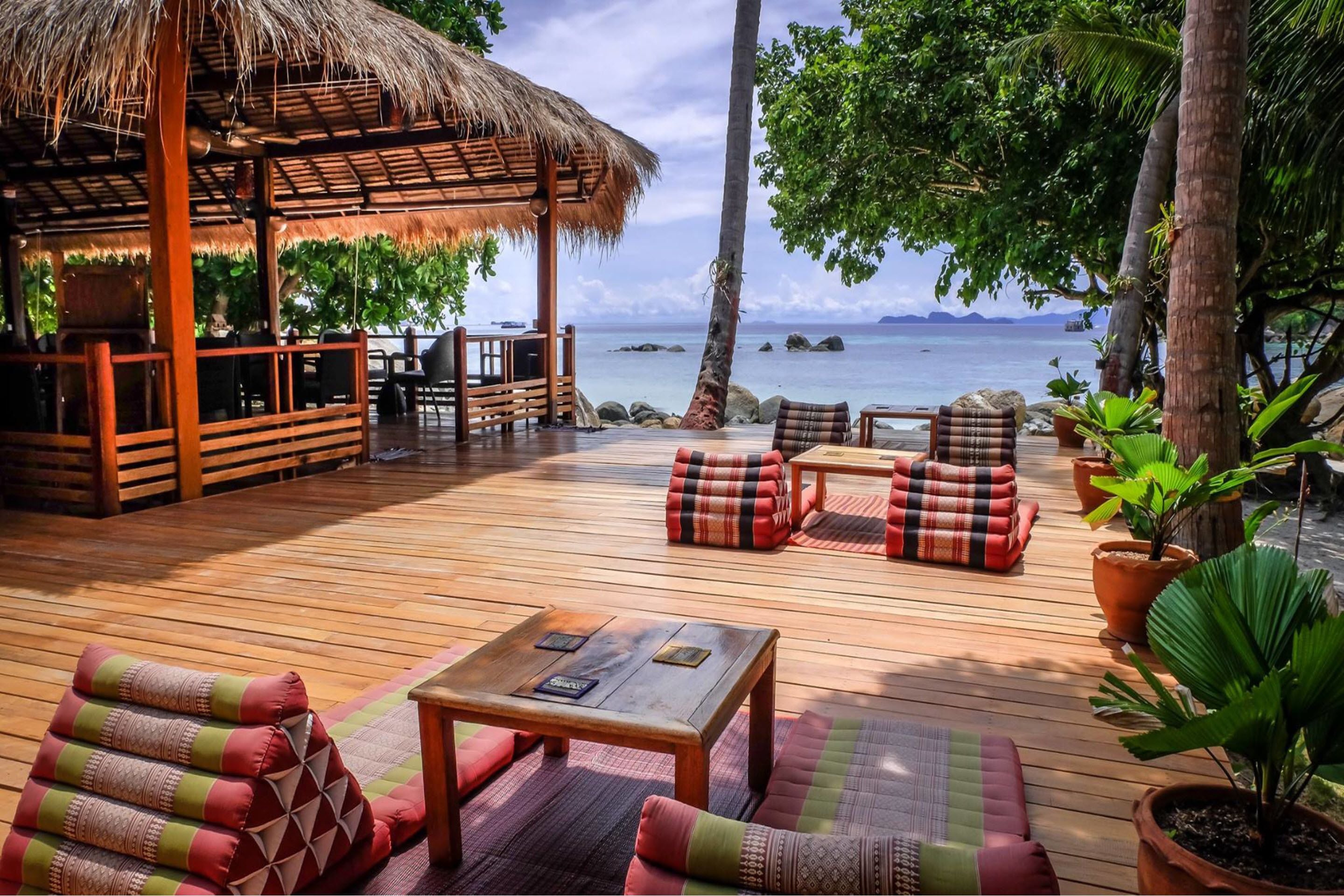 A wooden deck with seating, a thatched-roof structure, and potted plants.