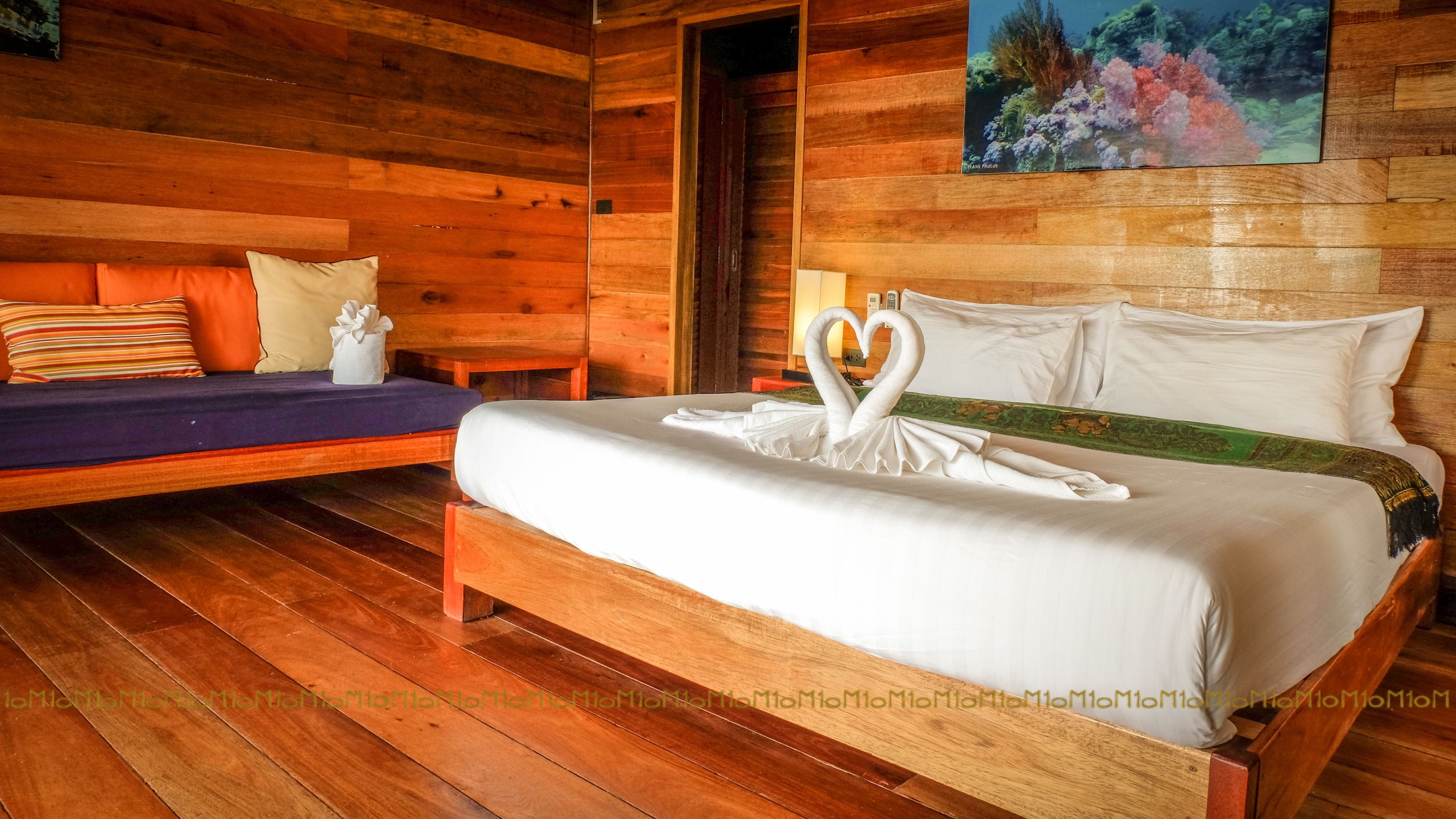 Ein holzgetäfelter Raum im Chalet-Stil mit einem Bett, das mit einer Schwan-Form-Kissenanordnung und einem Waldgemälde dekoriert ist.