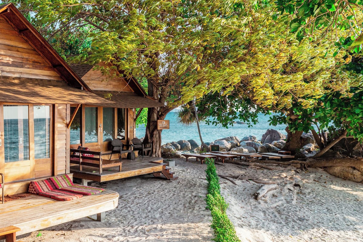 A wooden cabin with a balcony overlooking a beach, furnished with seating and a table.