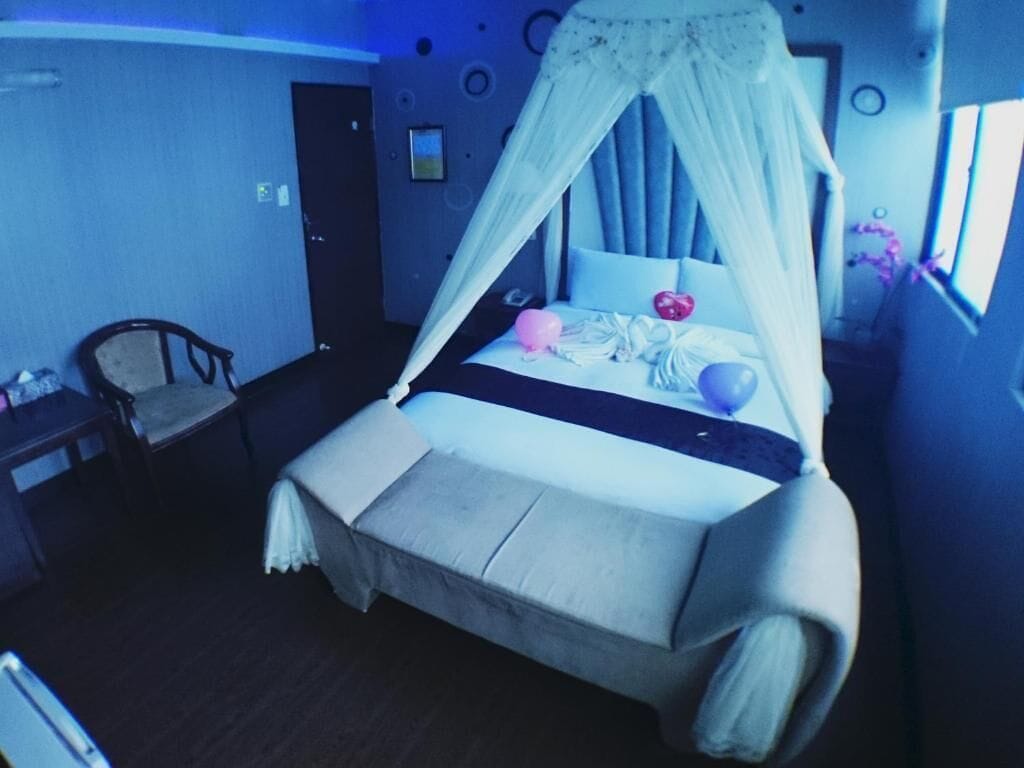 Ein Bett mit Baldachin, ein Nachttisch und ein Stuhl in einem Zimmer mit blauer Wand und Fenster.