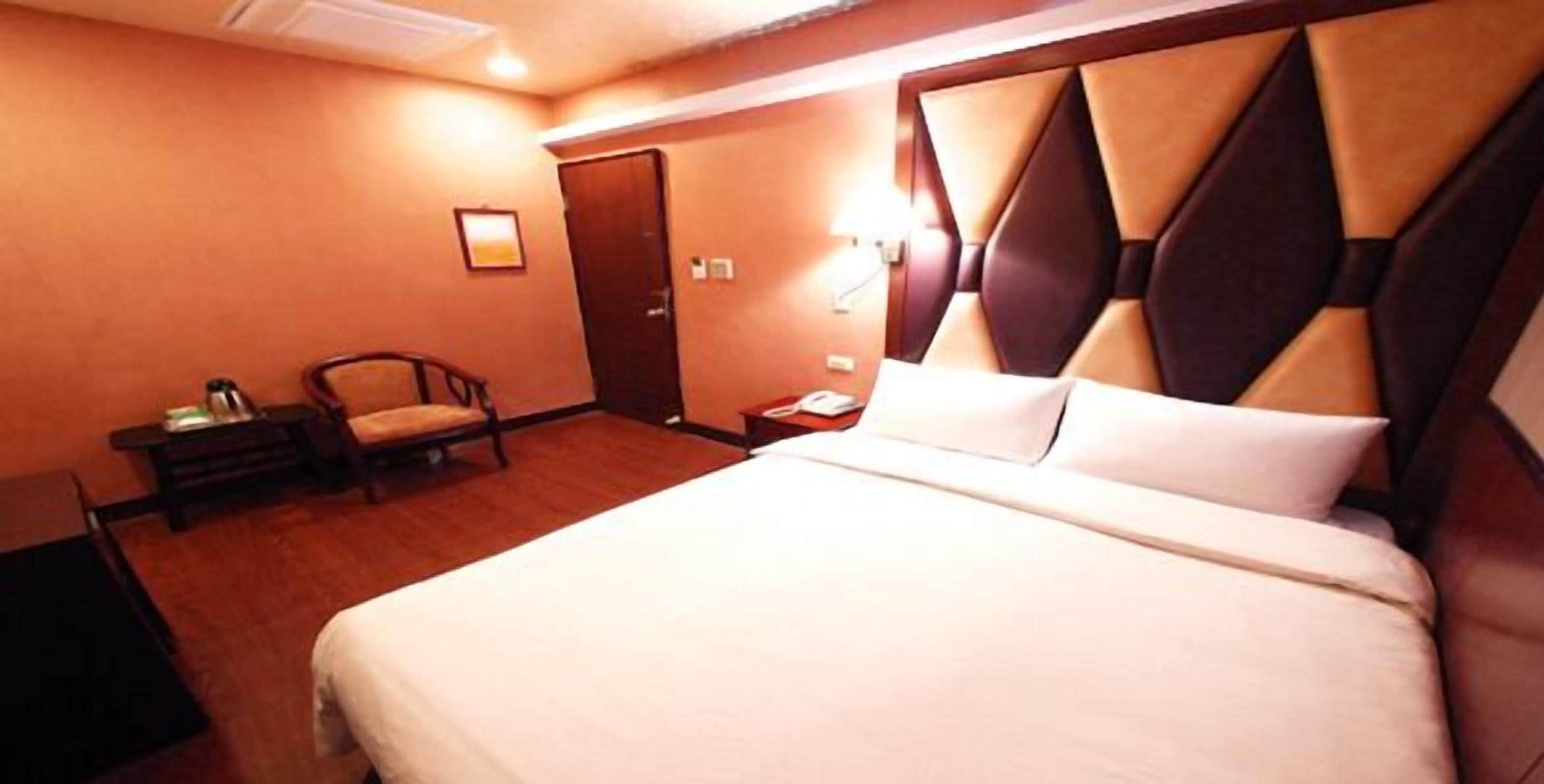 A hotel room with a large bed, a chair, a desk, and a nightstand.