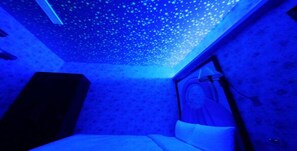 Una habitación con una cama, una mesita de noche y un techo con un efecto de luz de estrellas.