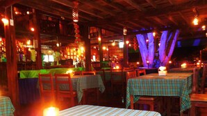 Un interior de restaurante con mesas y sillas de madera, iluminación tenue y faroles colgantes.