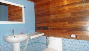 A bathroom with a wooden wall, a white sink, a mirror, and a toilet. - Zanom Sunrise Beach Resort (Koh Lipe)