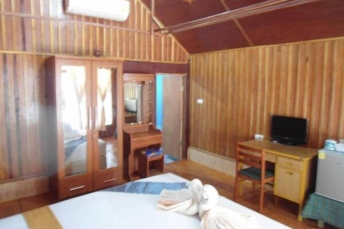 Una habitación con paneles de madera, una cama, un escritorio, un televisor y un armario.