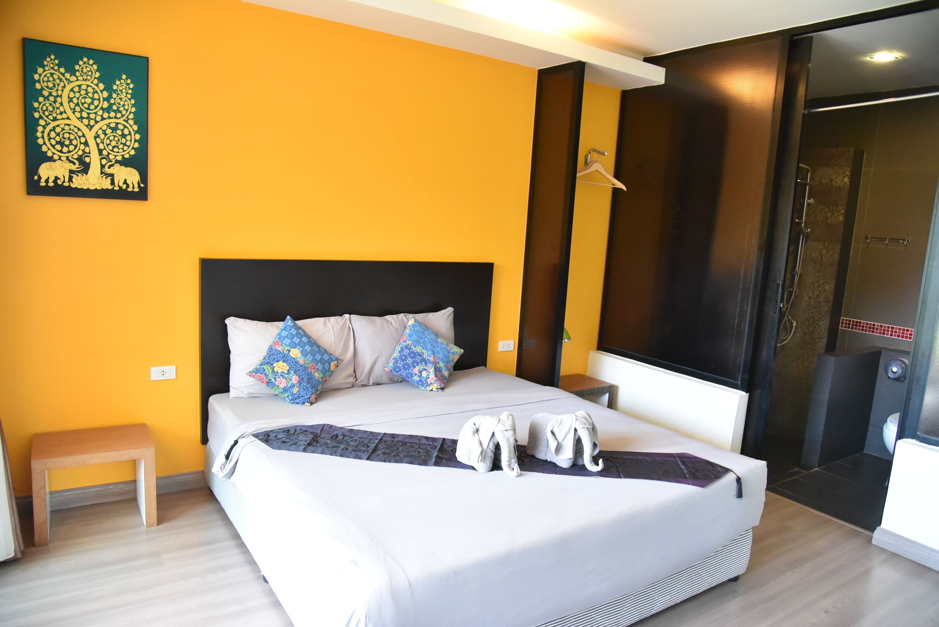 A modern hotel room with a large bed, a small bedside table, a bench, and a shower area.