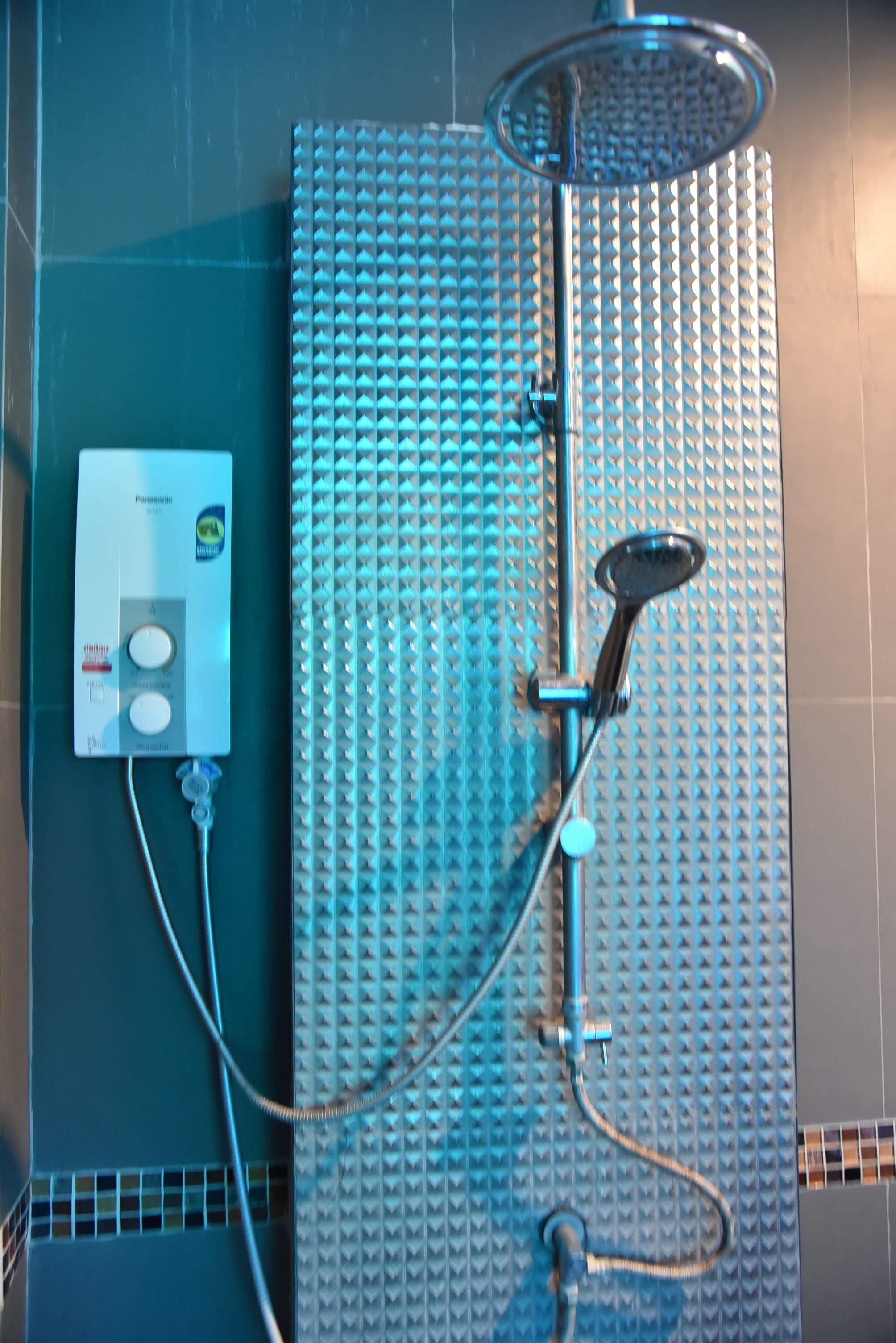 A shower with a control panel, a handheld showerhead, and a textured wall.