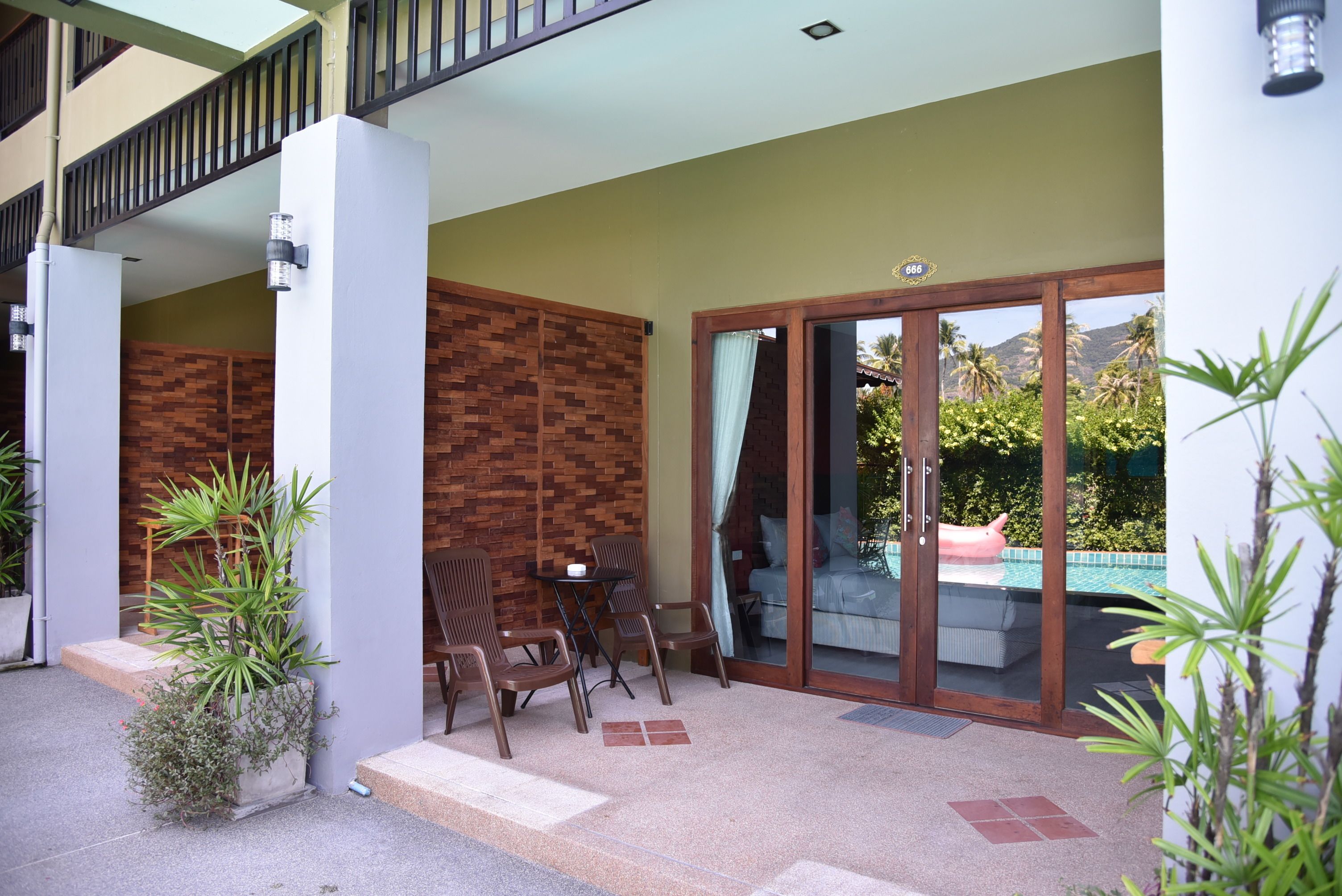 A covered outdoor seating area with a pool, wooden chairs, and potted plants.